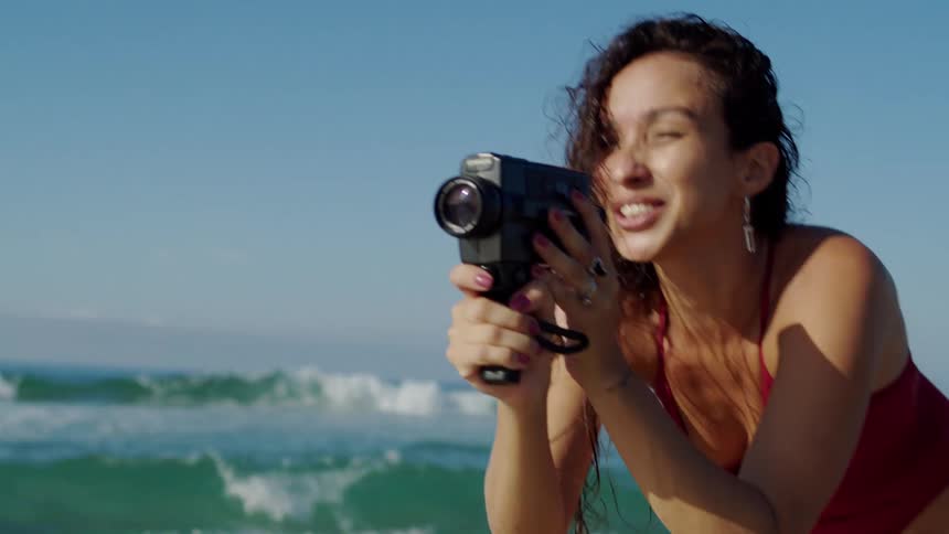 Smiling woman filming with a vintage camera by the sea