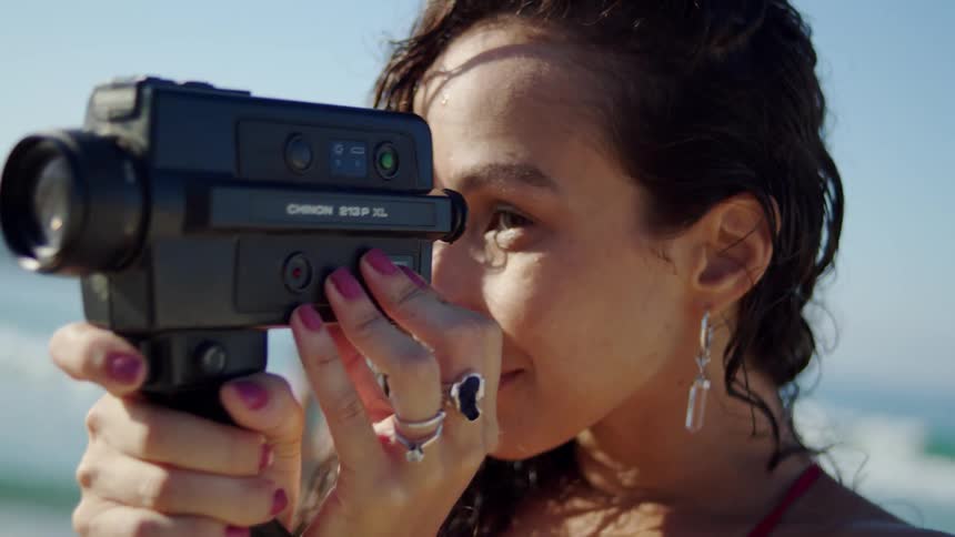 A person is holding and looking through a vintagestyle black video camera the persons right hand is on the handle and their left hand is adjusting the cameras zoom