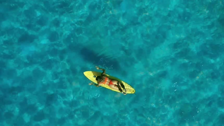 Woman in a bikini lying on her back on a surfboard in the blue sea