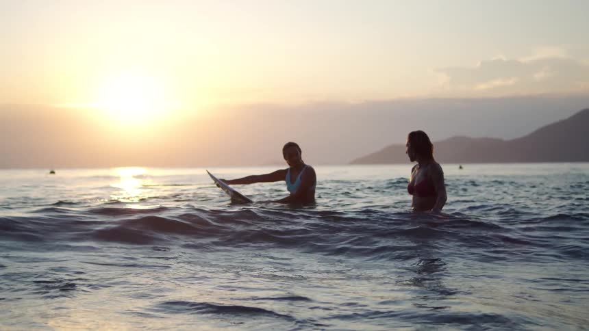 Two woman float atop their surfboards in the ocean at sunset