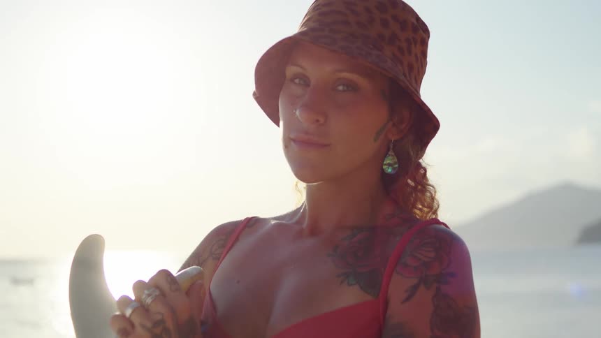 Woman wearing a patterned hat holding a surfboard by the sea