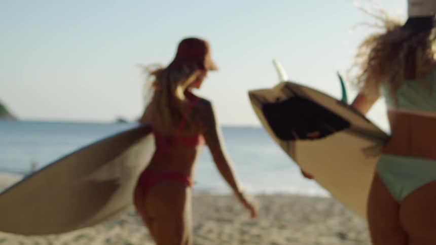 Two women running towards the beach water while carrying surfboards at sunset