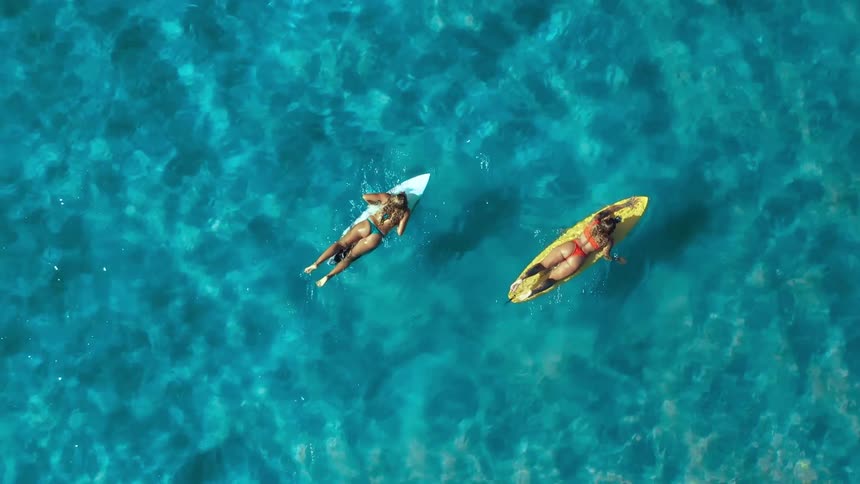 Two people surf paddle across clear blue ocean water