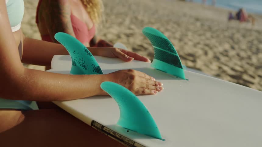Hands resting on a surfboard with blue fins on the beach sand