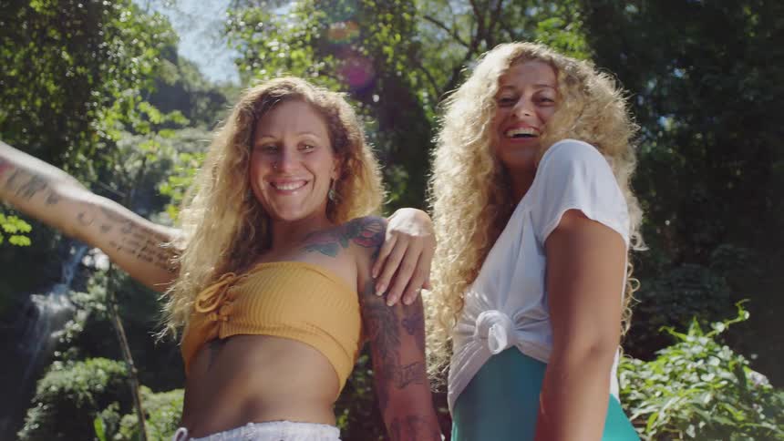 Two women smile in nature with a waterfall in the background