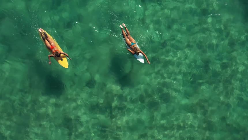 Two surfers paddle on their boards over clear turquoise water