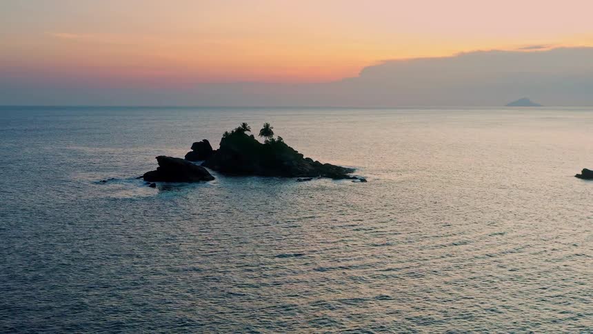 Small rocky island with palm trees surrounded by the sea at sunset