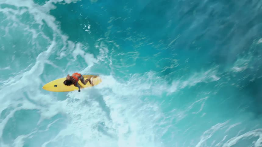 A surfer rides across bright turquoise waves on a yellow surfboard