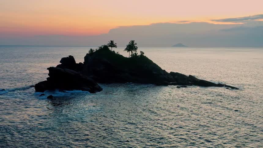A small rocky island is illuminated the setting sun creating a silhouette