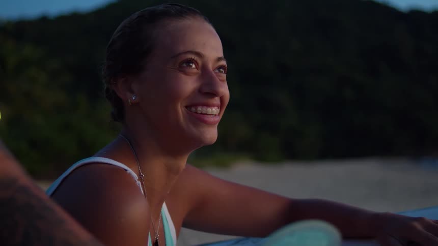 A young woman sits on the beach sand with friends having a good time and smiling