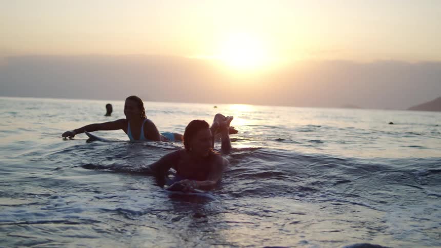 Two women float on their surfboards in the ocean