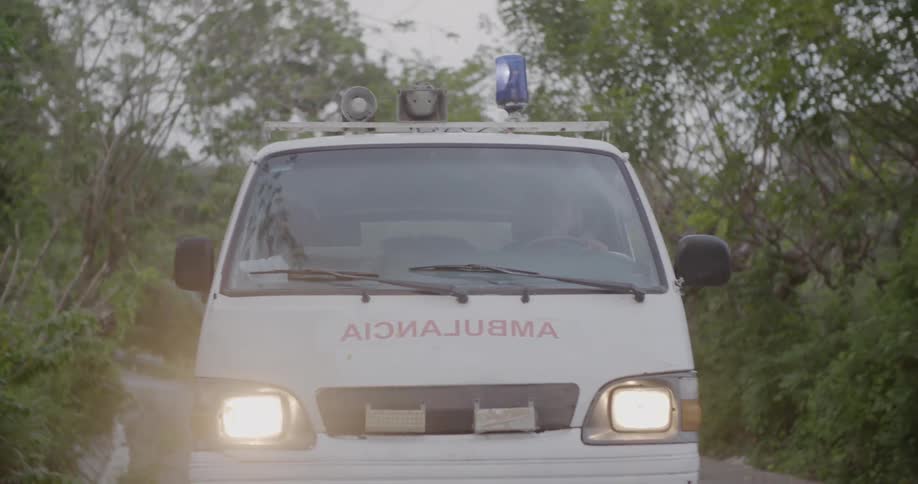 An ambulance has a flashing blue light as it drives down a road