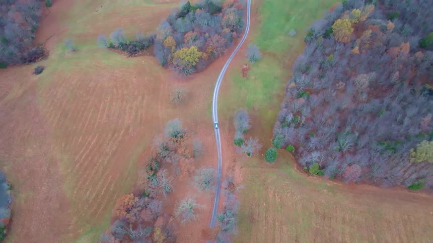 Birds eye view driving on a road across rural grasslands in the country in the fall