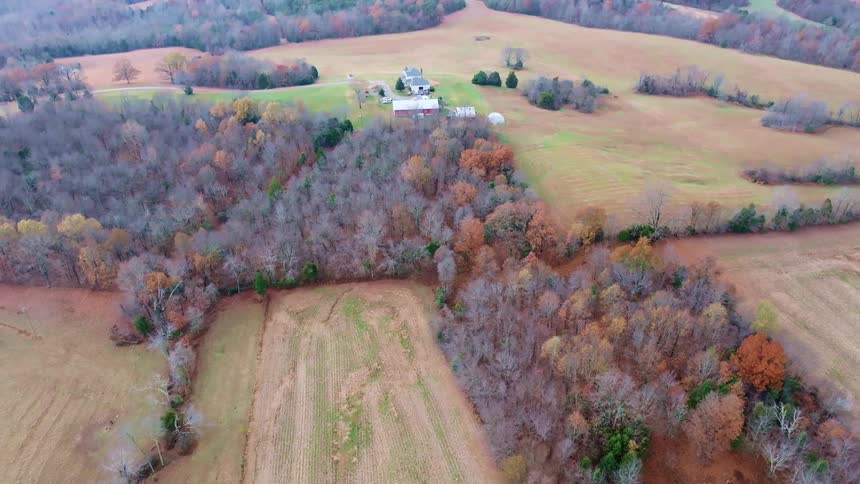 A farm nestled in a rural landscape surrounded by fields and a forest of trees in various autumn colors