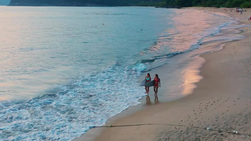 Two women walking by the sea with surfboards