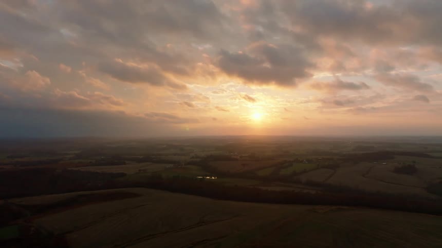 A wide expanse of land in a rural setting with the orange setting sun visible in the sky