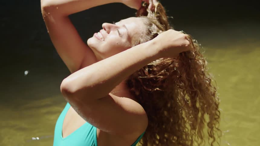 A woman with curly hair takes a bath in a stream wearing a bathing suit at midday