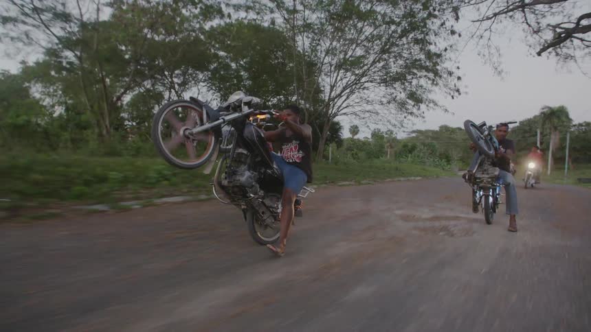 A group of people do wheelies on motorcycles down the street