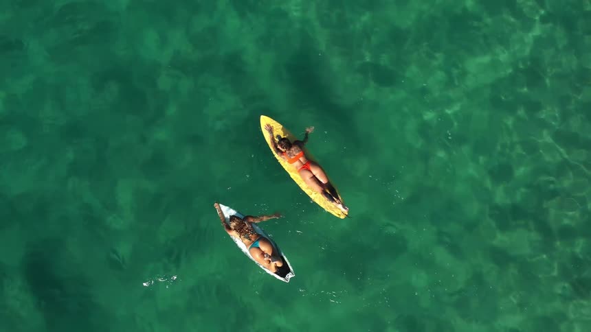 Overhead view pair of female surfers floating on surfboards in the ocean