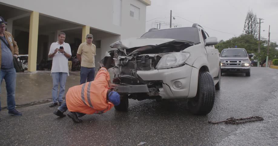 A tow truck worker is attaching a chain to a wrecked vehicle