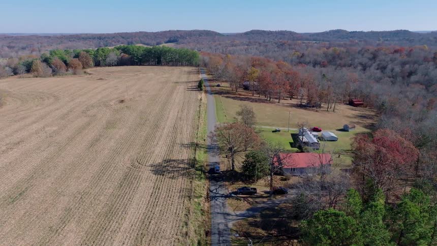 Car drives along a narrow road between a harvested field and wooded area
