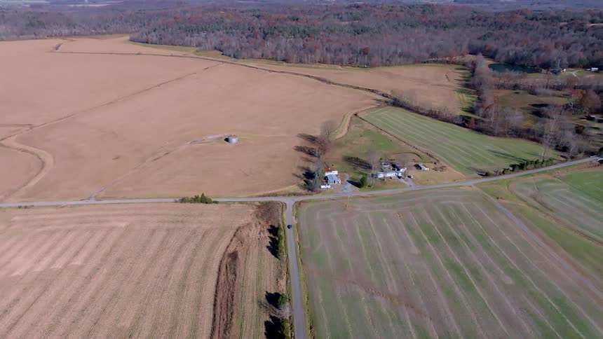 A car drives along a rural road near a farm on a sunny late autumn day