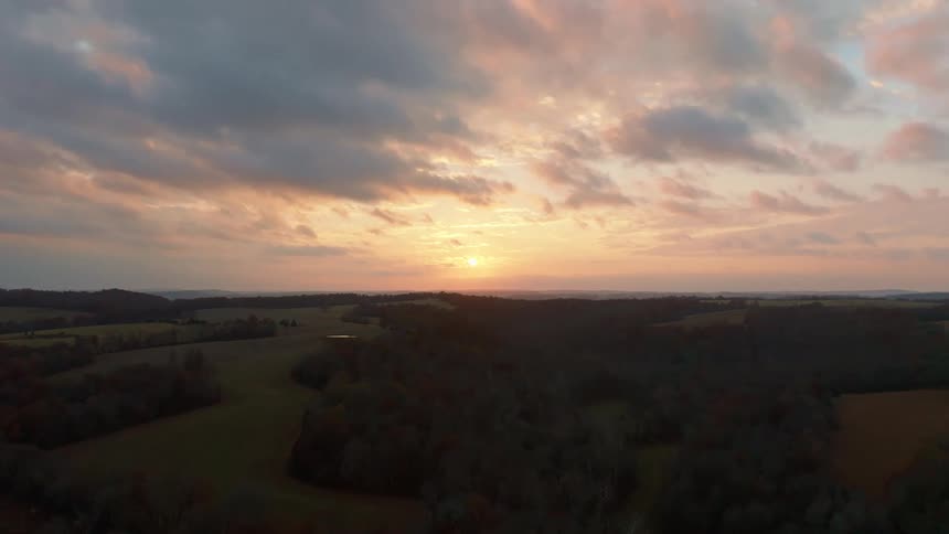 A rural setting featuring a wide expanse of land partly covered with trees and sparse buildings at sunset