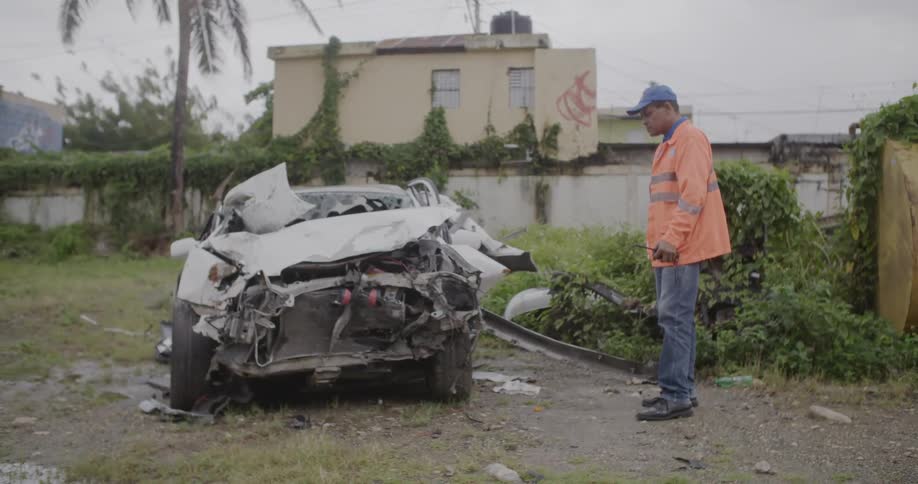 A man wearing an emergency jacket is looking at a badly wrecked vehicle