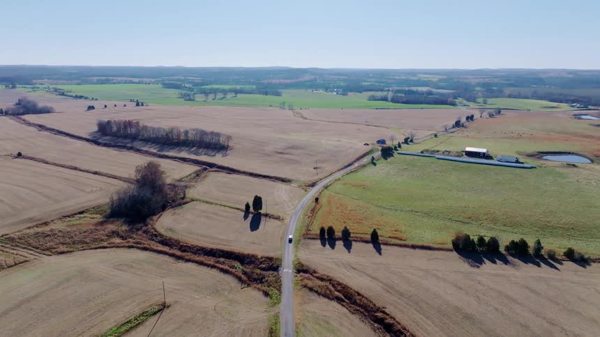 Aerial view of a country road winding through wide farmland fields