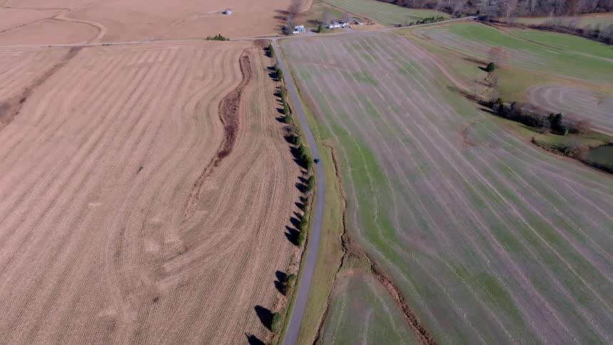 Rural road flanked by dry and green farmland seen from above