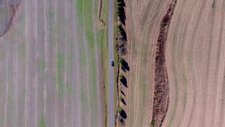 Aerial view of a car traveling down a narrow road surrounded by rural fields