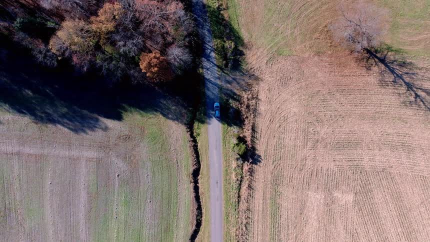 Aerial of a blue car driving along a rural road near farmland