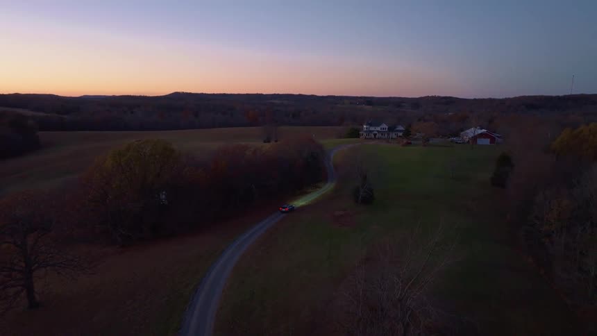 The car is driving on the dirt road towards the farm
