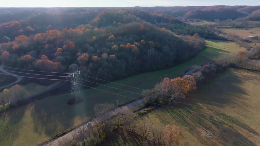 A power line stretches across a forested area with a freeway connecting rural communities as a car drives by at midday
