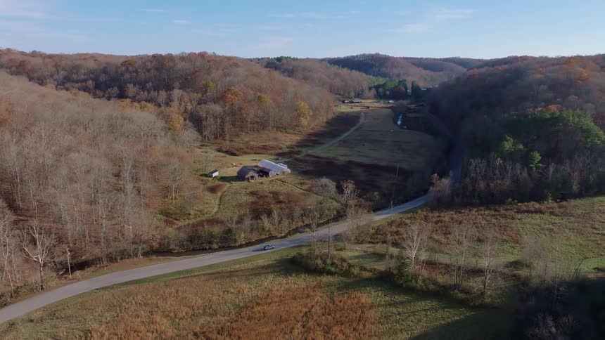 A rural road winds through a valley with autumn hills