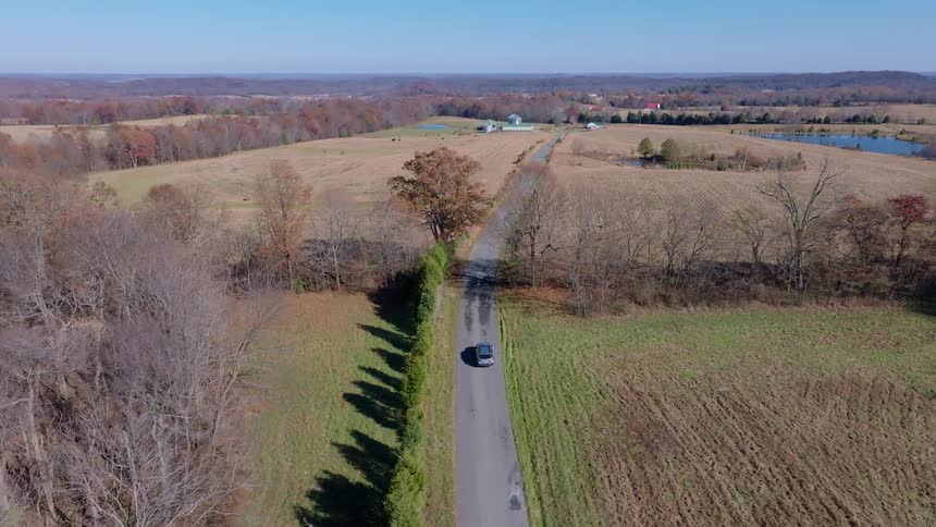 Aerial view of a car driving down a narrow country road through farmland