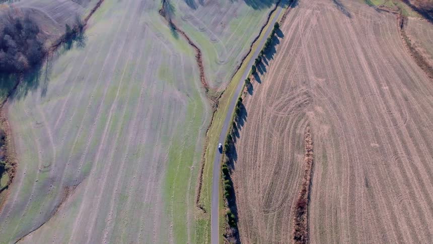 Aerial view of a car driving along a country road in rural fields