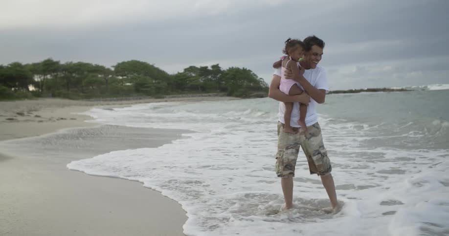 A man is holding his toddler child and playing in the surf