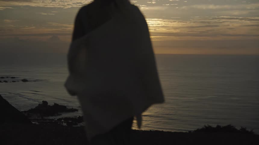 The video shows an aerial shot of a sun setting over the ocean a cloudy sky and the glinting sun can be seen reflected on the water