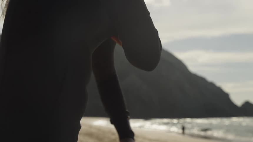 A woman pulls on the sleeve of her wet suit while putting it on
