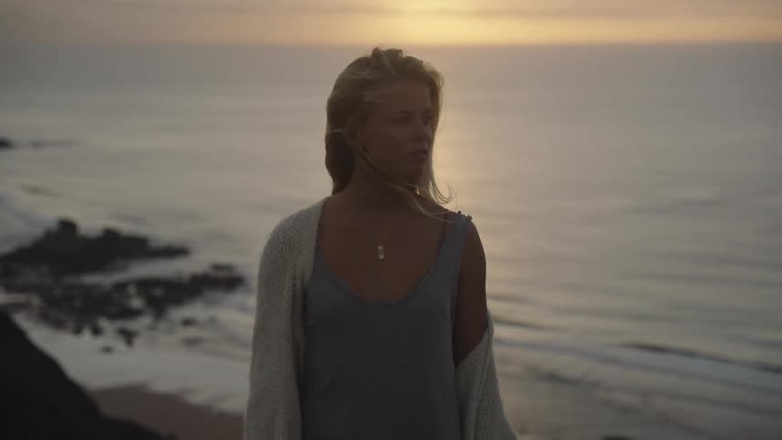 Young woman standing along the coast as the sun sets on the horizon