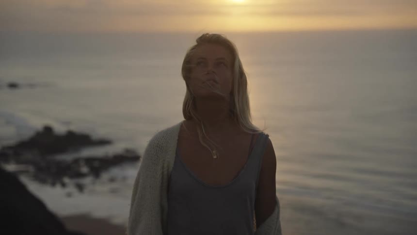 Woman gazes at the sea at dusk with the wind blowing through her hair