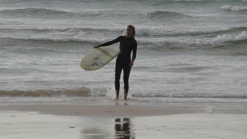 Female surfer walking out of ocean carrying her surfboard