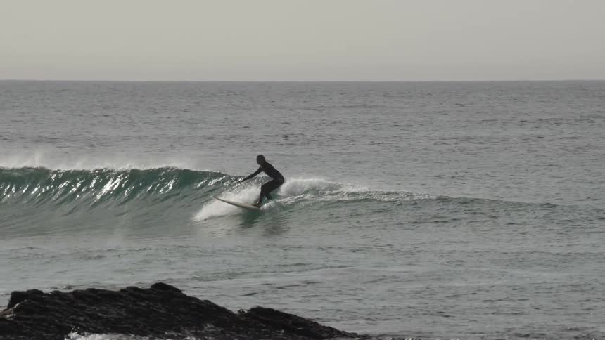 Person surfing a small wave in the sea near rocks by the shore