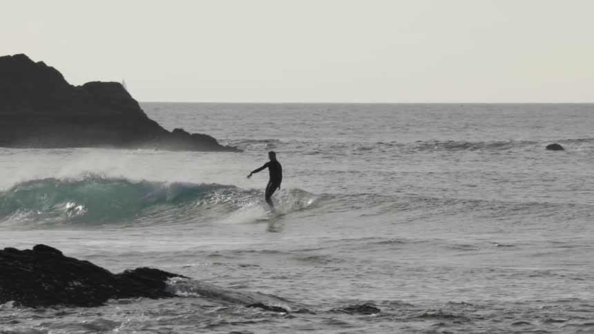 Surfer riding a wave near rock formations in the sea