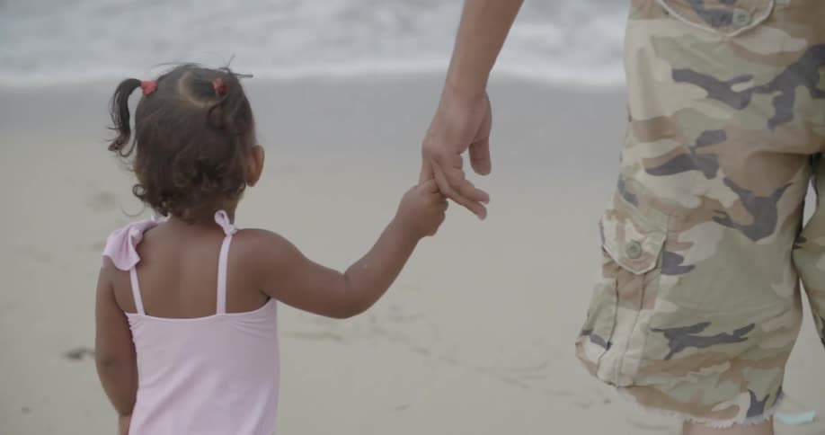 Man and toddler girl holding hands walking on beach