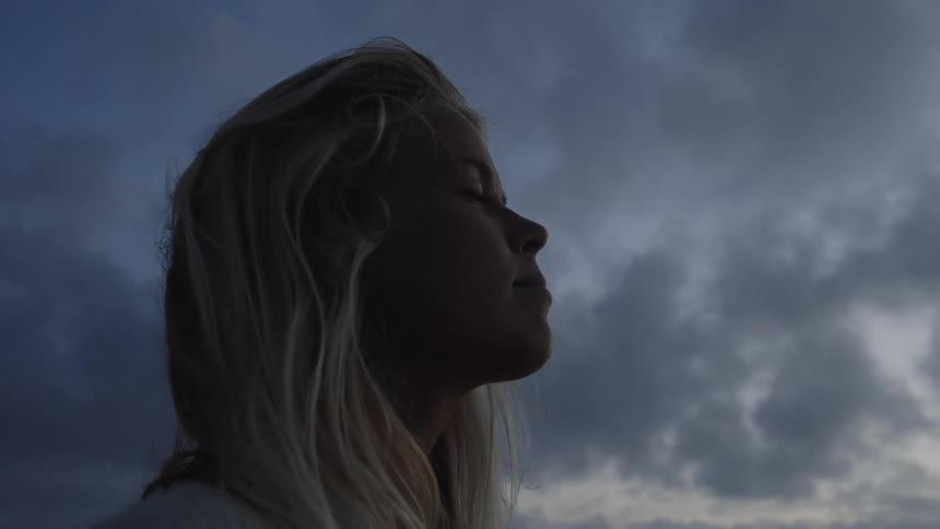 A person with blonde hair is shown from the side looking towards the sky the background features a cloudy dark sky suggesting dusk or dawn