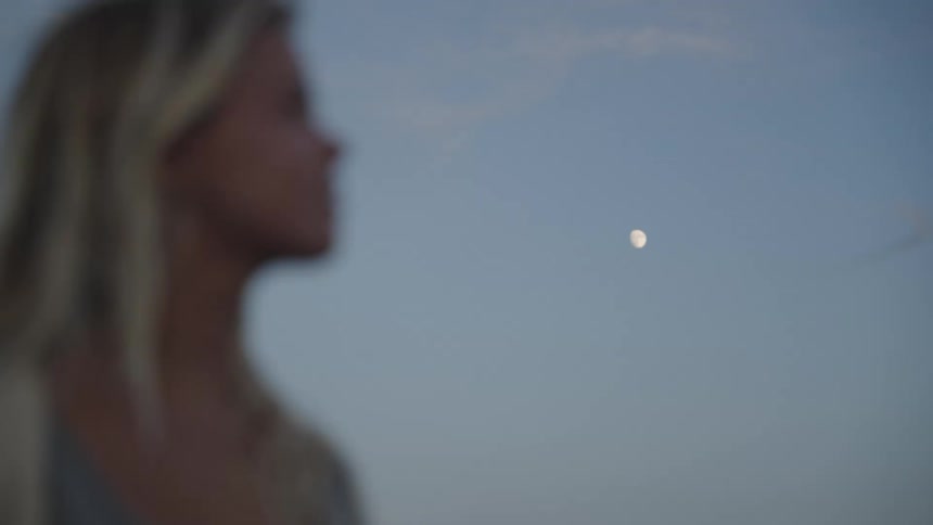 Woman blurred in the foreground looks at the moon in the blue sky