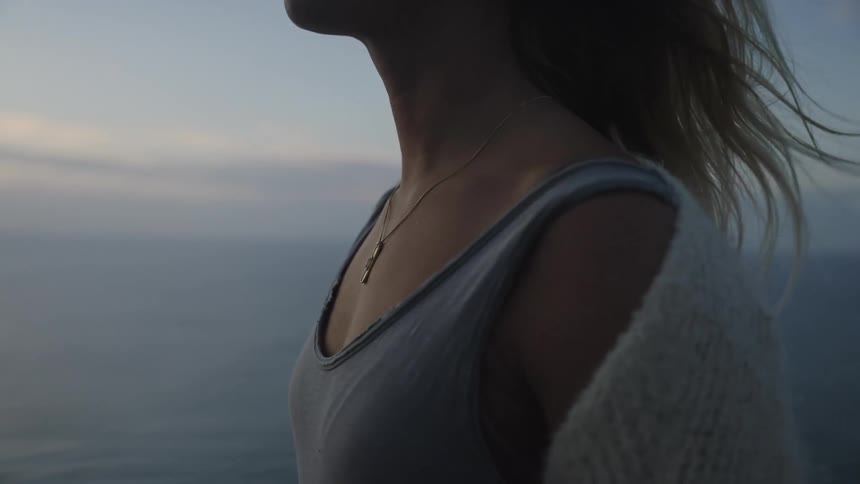 A young woman stands on a hill by the shoreline wearing a necklace at midday