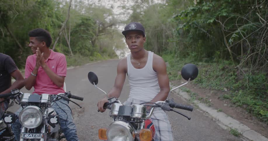 A group of men sit on motorcycles on a road in a jungle